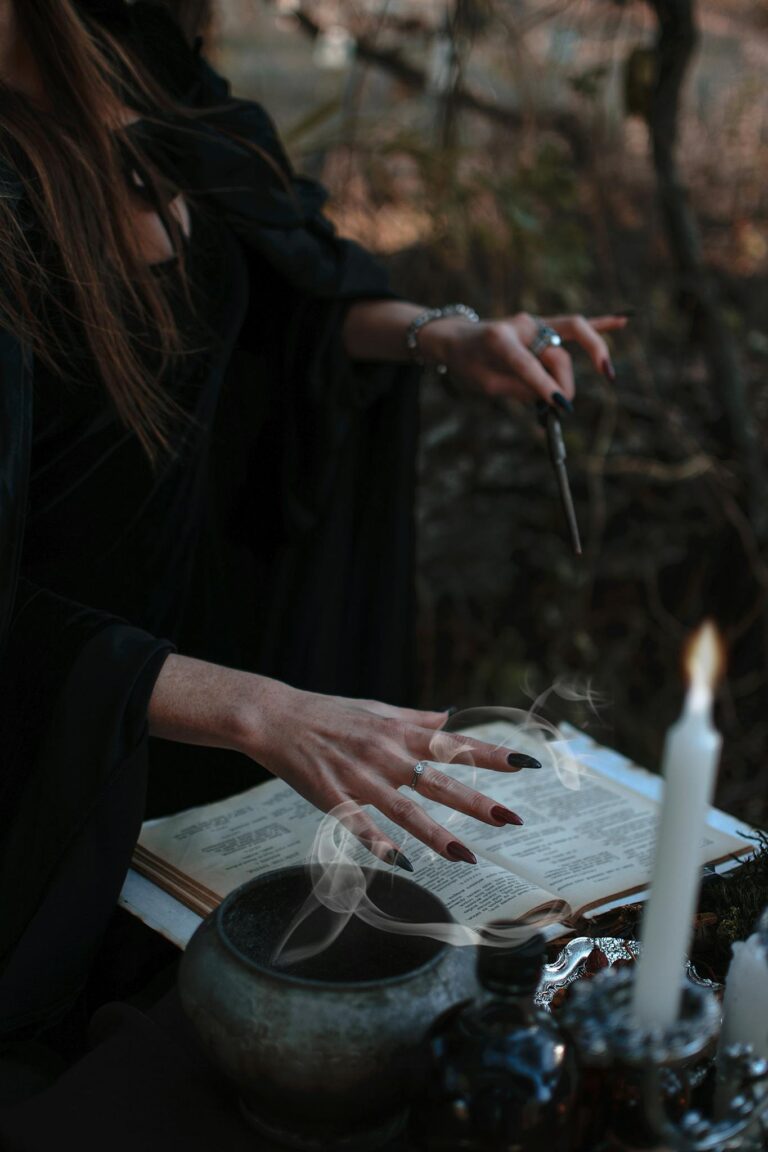 A shadowy witch performs a ritual with book, smoke, and candles outdoors.