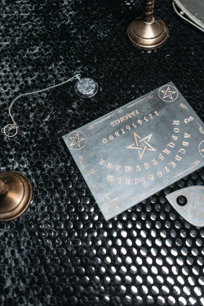 Top view of a mystic Ouija board with pendulum on a textured black surface, creating a spiritual atmosphere.